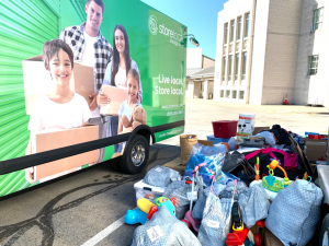 Stack of donated items next to a truck with a graphic of a family holding moving boxes