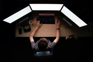 Photographed from above shows a human in front of three large computer screens.