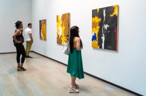 Three people look at three abstract paintings on a wall by artist Clyfford Still