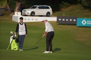 Watched by his caddy, Chinese male golfer Yue Liu plays a shot from the fairway at the Volvo China Open