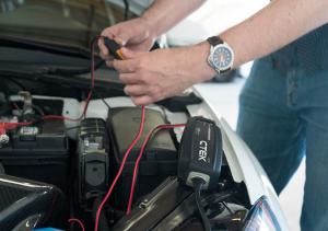 Hood of car open with the battery attached to a CTEK MXS 5.0 battery charger.