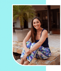 Rae the Anxiety Coach is expressing happiness as she sits comfortably near a fountain