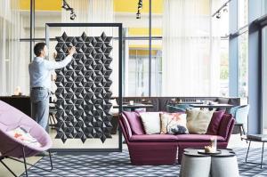 Freestanding Room Divider Facet by Bloomming, used in a restaurant or bar setting. A person is seen adjusting the individual diamond-shaped elements to create a new pattern.