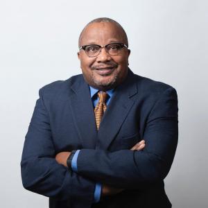 Official headshot of Louis J. King II the new New President and CEO of OIC of America. Louis is wearing a navy blue blazer, light blue dress shirt and tan tie.