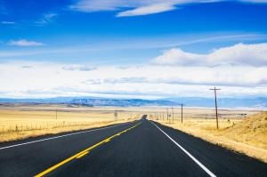 A New Mexico Roadway leads towards the mountains between amber colored fields. (Credit: Kelly Pierce/Route Three Productions)