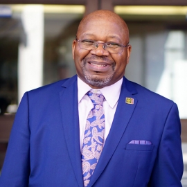 Smiling man with glasses, wearing blue suit and tie, white shirt