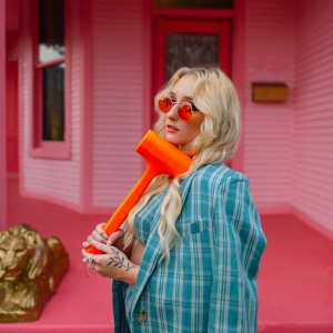 Artist Juliana Hale in front of pink house holding a prop.