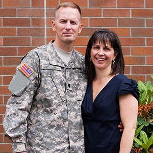 A man in an army uniform and a woman pose for a photo, arm in arm