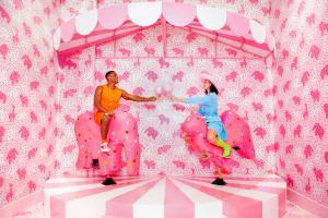 Two people cheers with cotton candy was they ride on a pick animal cracker carnival ride at Museum of Ice Cream in Austin, Texas