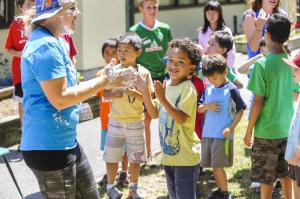 Young child looks at the camera while smiling and clapping during a camp activity.
