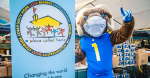 Los Angeles Rams mascot Rampage stands next to banner with A Place Called Home logo on it