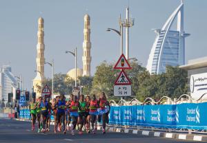 A group of elite male athletes running together along a road in front of Dubai buildings including the Burj Al Arab hotel
