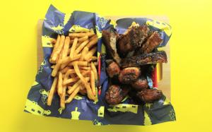 An image of ribs and fries sitting in food baskets lined with food paper featuring an outdoorsy design in blue and yellow.