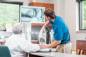 The Micro C portable x-ray system is being used in a clinic to take clinically relevant x-ray images of a patient's hand and wrist. The images are displayed on a screen for both the patient and the clinician to view.