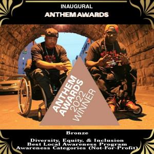 2 black guys sitting in wheelchairs from Paraplegic rap group 4 Wheel City. Under tunnel wearing black jeans and tee shirts, with hats turned to the back, holding up 4 fingers