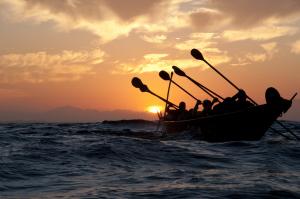 People paddling in vessel as sun sets on Pacific Ocean