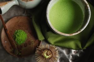 Looking down on the preparation of a matcha latte including the powder and whisk used to create the product