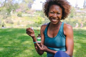 African American Woman At The Park Holds Brown Glass Bottle and Pipette Filled with CBD Oil Tincture