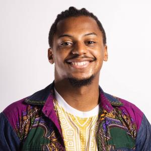 A profile picture of a smiling Ezra Bristow in a yellow shirt under a patterned shirt