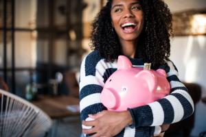 Black young woman hugging her pink piggy bank