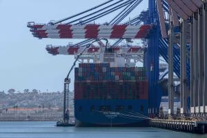 Ship up against a dock with large containers stacked on the deck