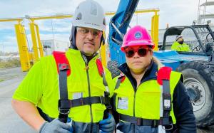 Aaron Borrero stands next to Mari Borrero, both wearing construction hard hats and high visibility vests