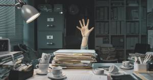 Work From Home Stress. Person behind desk is drowning. One hand up is asking for help. Desk is loaded with piles of paper and empty coffee cups. File folders are everywhere.