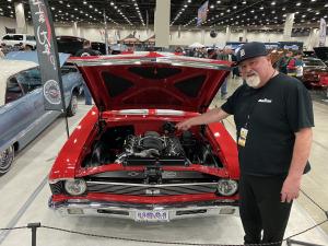 Larry Beers standing in front of his red 1970 Chevy Nova with the hood open at Autorama 2022