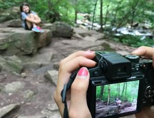 Photo of a person using a camera to take a photo of little girl sitting on rock in state park
