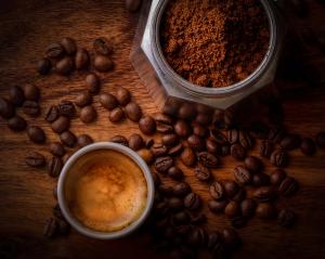A picture of a cup of coffee with some coffee beans and ground coffee.