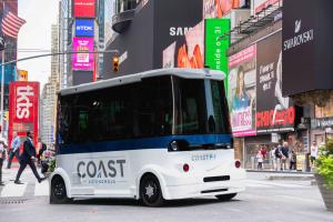 COAST P-1 Shuttle in the middle of Broadway in Times Square, New York City with pedestrians walking behind the vehicle.