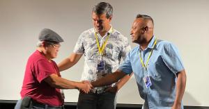 Shareef Haq, Fred Jee, and Eladio Arvelo embrace on the theater stage in front of film screen.