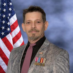 Photo of Mark Napier with American flag in the background wearing his four top US Army medals, a CIA lapel pin and U.S. - Afghan flag lapel pin.