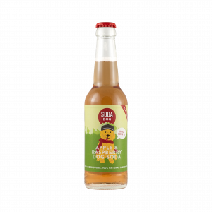 A soda bottle for Soda Dog, a craft sodas for dogs, in Apple and Raspberry flavor. The bottle has a label with an illustration of a shaggy dog covering most of it, but the bottle beck is clear showing an apple coloured liquid.