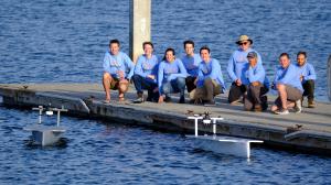 The Seasats team stands on a pier next to two autonomous surface vehicles in the water