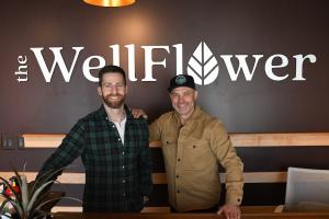 two men standing at the inside of a cannabis shop with a store logo behind them