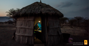 Twelve-year-old Musa Simon uses one of the family's solar lamps to study at night in the family hut in Tanzania. He is sitting in the hut lit by the solar lamp, and it is dark all around. He lives in the savannah in Tanzania.