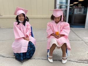 Two Evergreen Academy Preschool students dressed in pink cap and gowns are excited for their graduation from preschool.