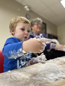 An Evergreen Academy Preschool student is having fun with his hands and table covered in foam.