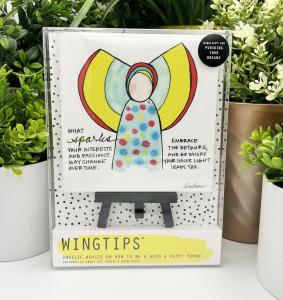 The WingTips for Pursuing Your Dreams collection is packaged with a wooden easel in a clear gift box. The whimsical angel image at the center of the print appears to be wearing an aquamarine dress with large, irregularly spaced red, yellow and teal dots. 