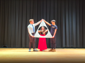 2 students hold up a triangle with a hole while another sings in the middle of it.