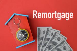 Money banknotes, toy house, compass over red background written with REMORTGAGE