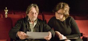 Two people sit in theatre seats with an Oscar statue nearby