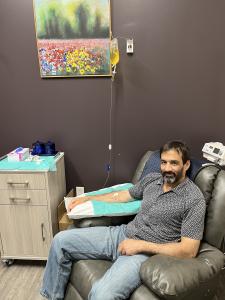 Handsome middle aged, slender man sitting in a reclining chair with an IV in his arm connected to a yellow bag with nutrients.