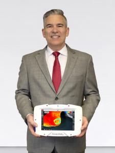 Kent's CEO, Pierre Lemire, wearing a grey suit and red tie, front facing with medical device with SnapshotNIR