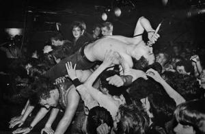 Jello Biafra of the Dead Kennedys, shirtless, on his back, being held up by a crowd while singing into a microphone