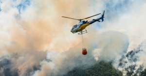 Helicopter in-flight carries a water dispersing system over a burning wildfire