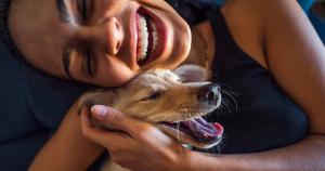 A woman is laughing and hugging a dog. The dog looks happy and relaxed.
