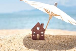 Miniature house and umbrella on beach, blue sea and sky on blurred background