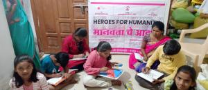 Children sit around a woman, also seated on the floor. They are learning about primary health and hygiene as part of the Heroes for Humanity initiative in India by The Desai Foundation.
